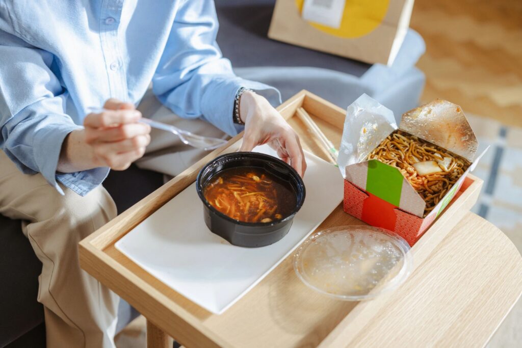 Comfortable home food delivery: person eating Asian food and soup from takeaway containers on a tray