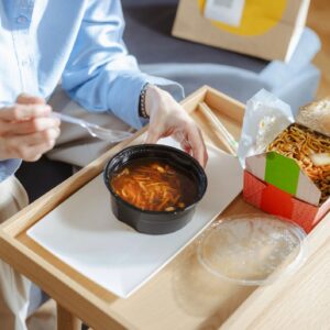Comfortable home food delivery: person eating Asian food and soup from takeaway containers on a tray